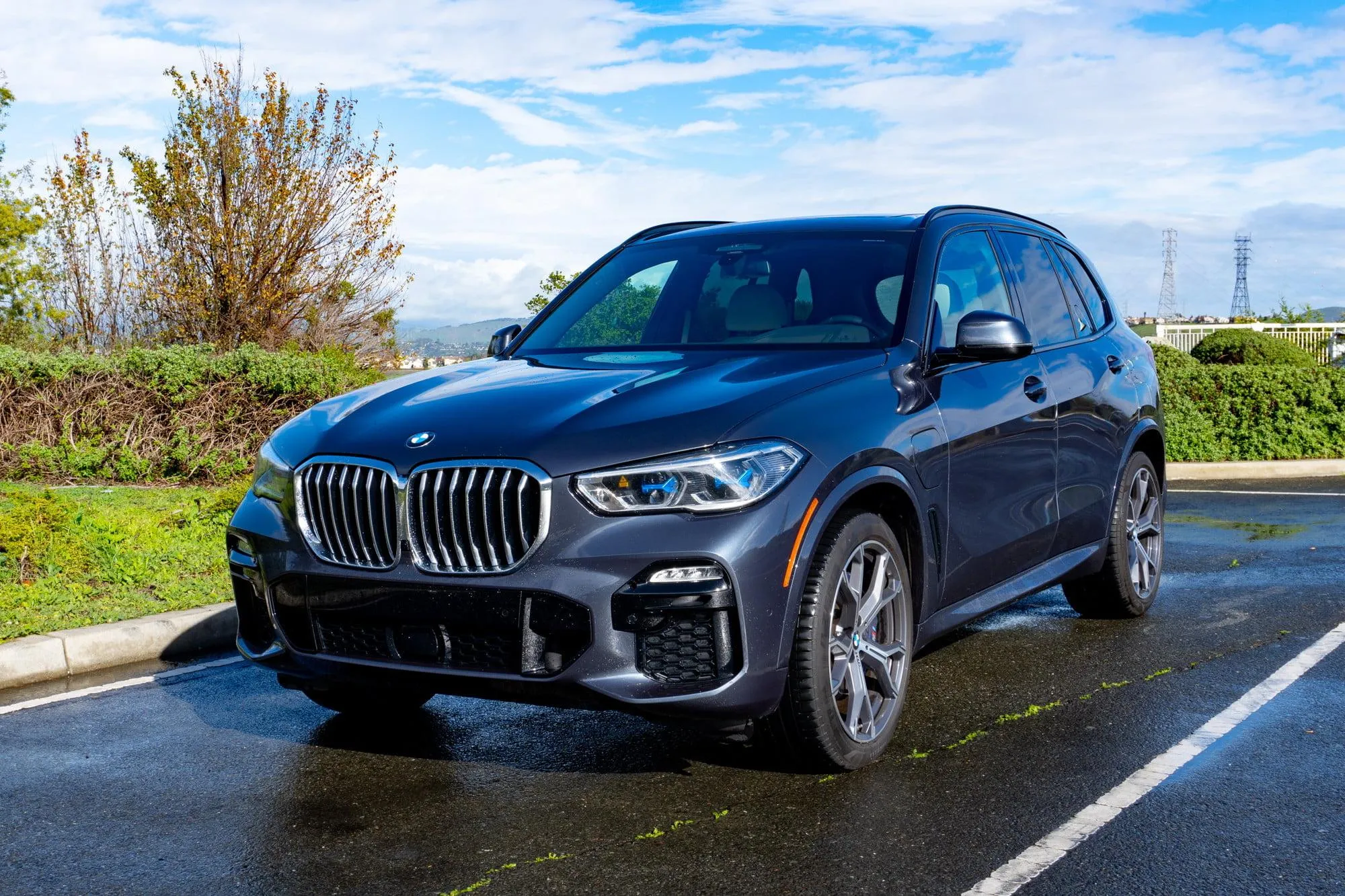 Dark Bmw Suv on Wet Road Reflecting Trees and Sky Image
