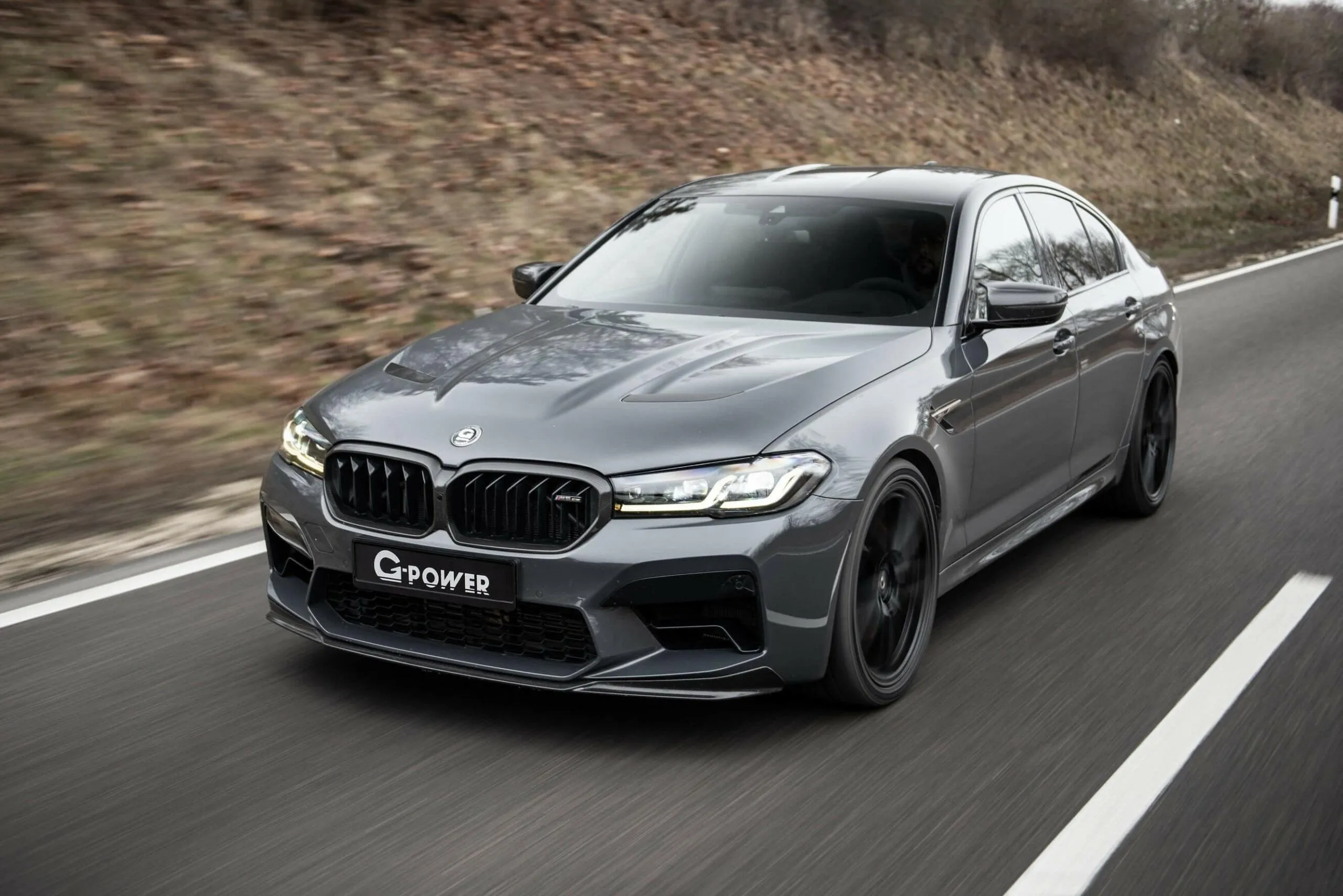 Grey Bmw Driving Fast on Winding Road Near Forested Hill