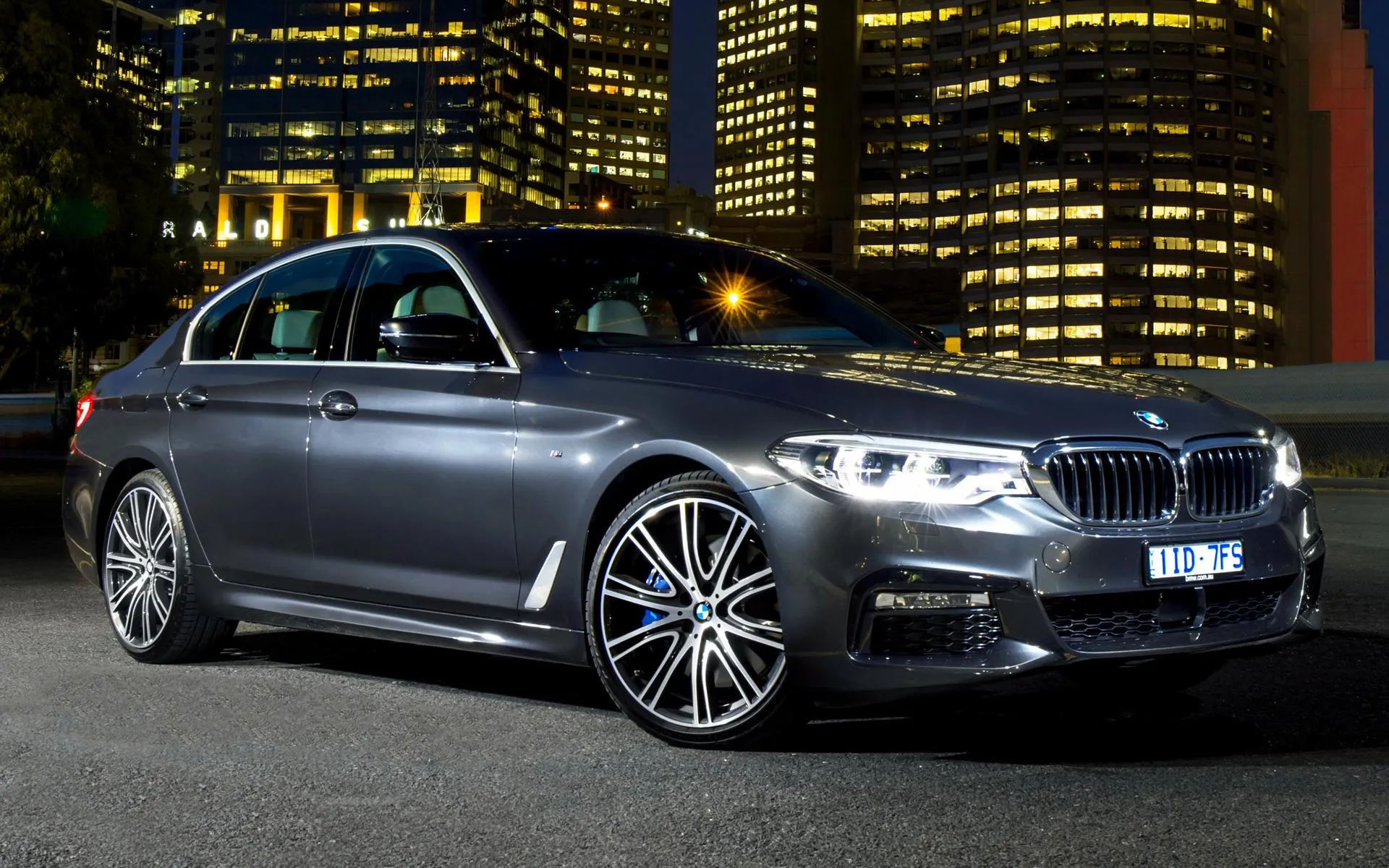Luxury Bmw Sedan Parked with City Lights Behind Wallpaper