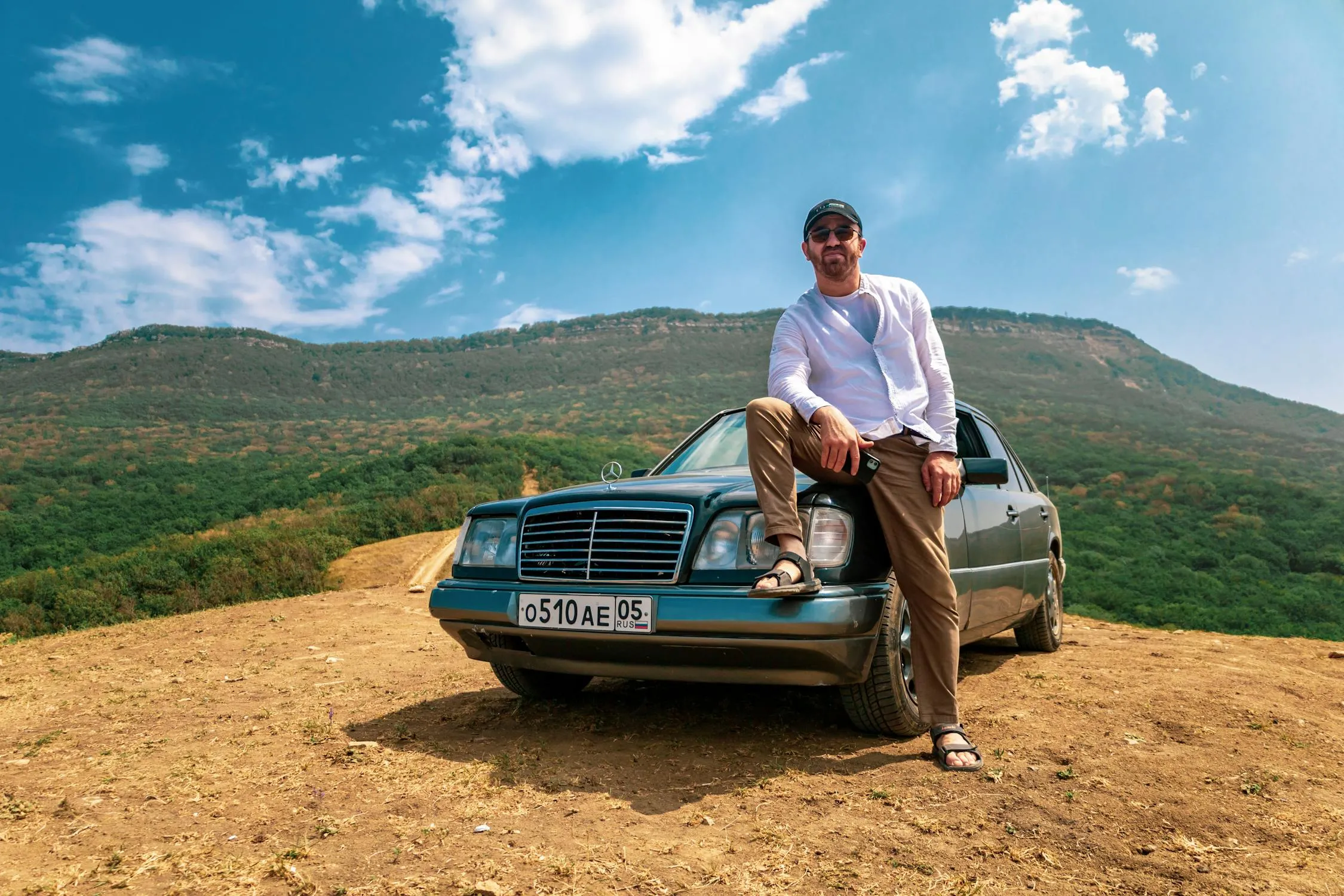 Man sitting on hood of a vintage Mercedes Benz in countryside
