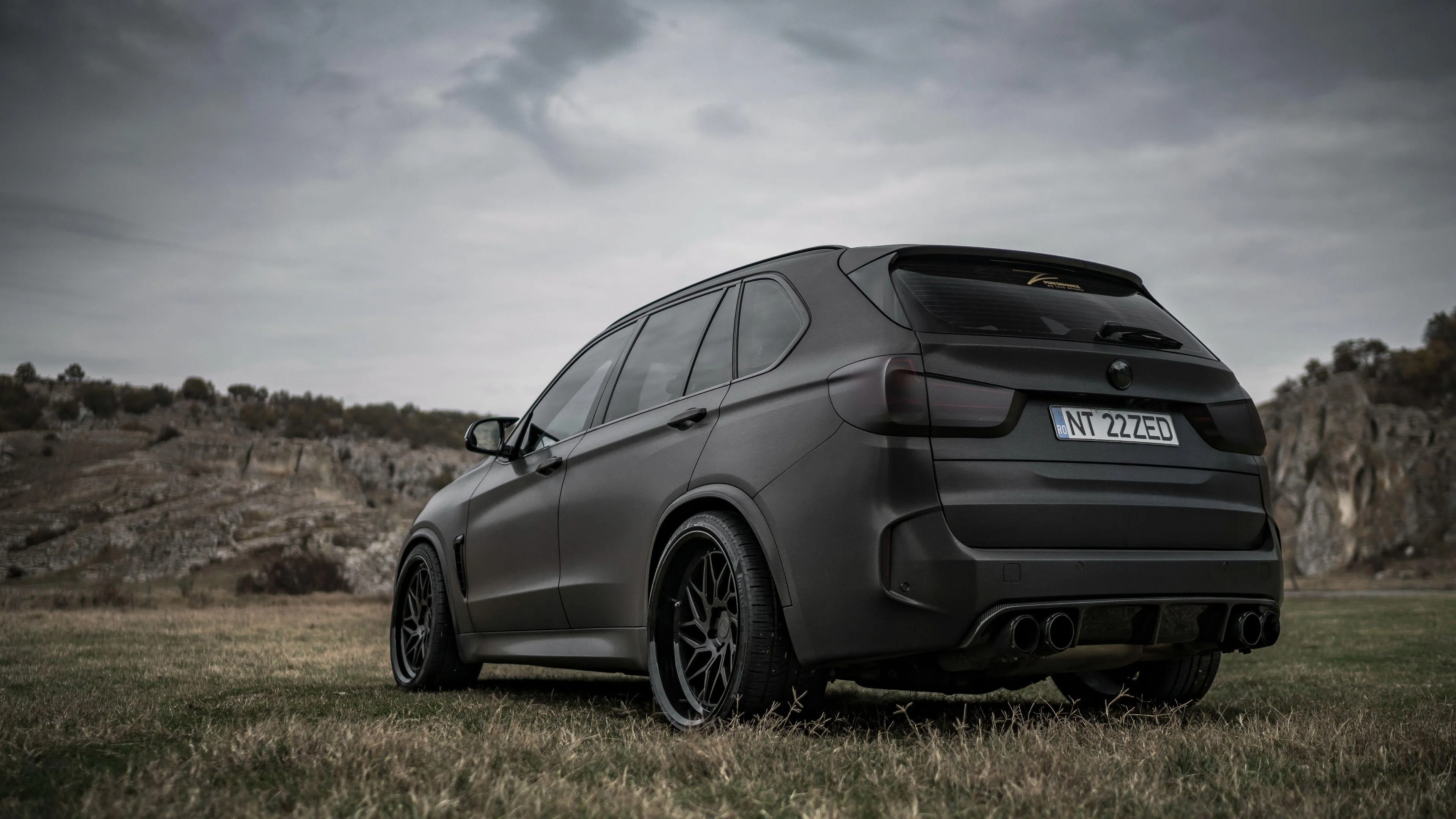 Matte Black Bmw Suv in Rugged Outdoor Terrain Wallpaper