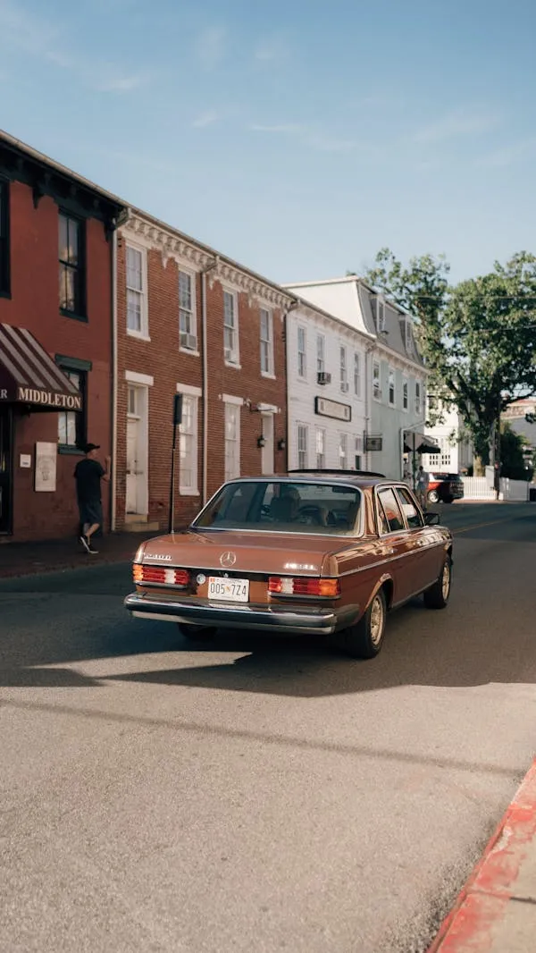 Old Mercedes sedan cruising down quiet small town road