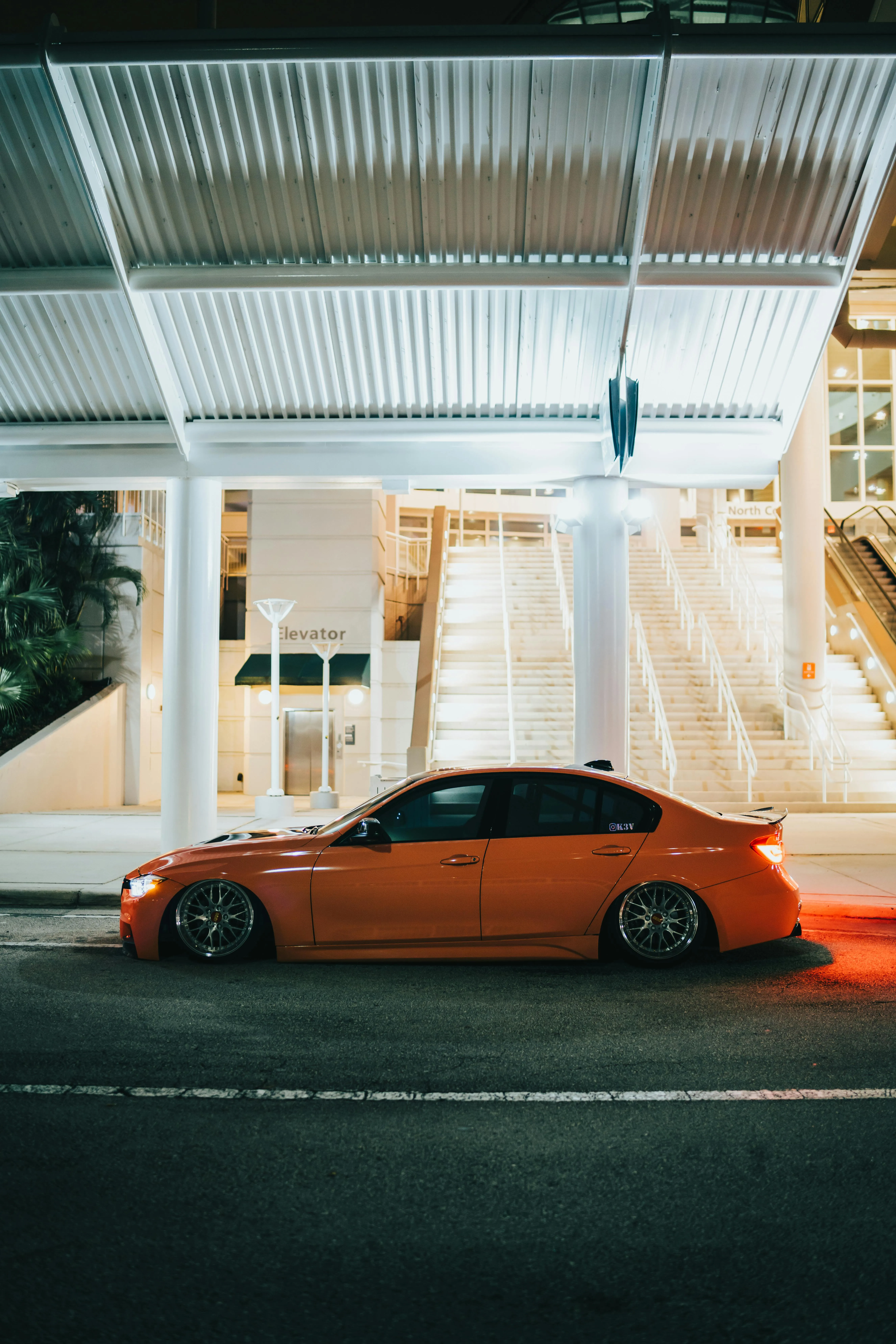 Orange Bmw Seen Under a Lit Modern Structure at Night