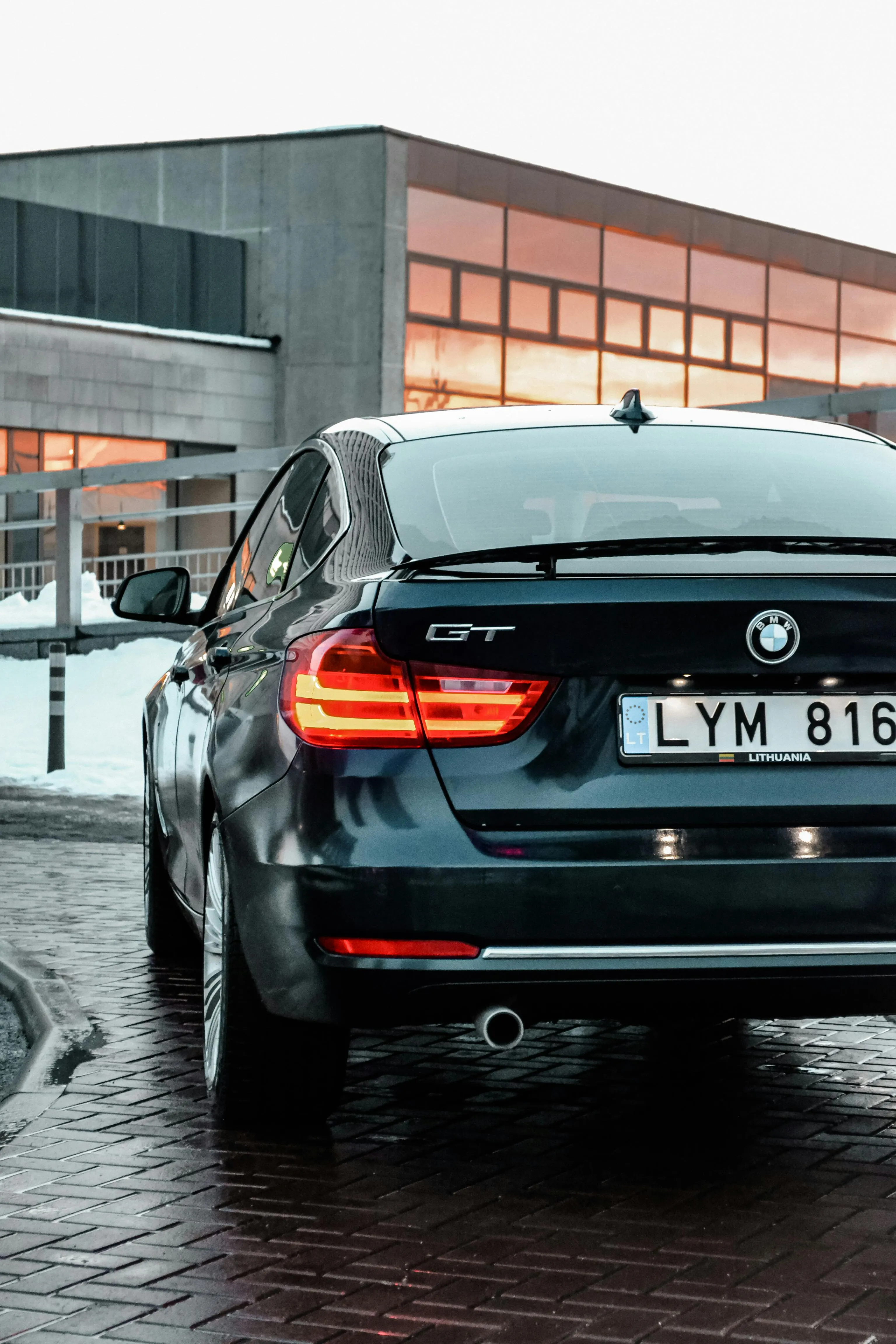 Rear View of Bmw Driving on Wet Urban Street By Building