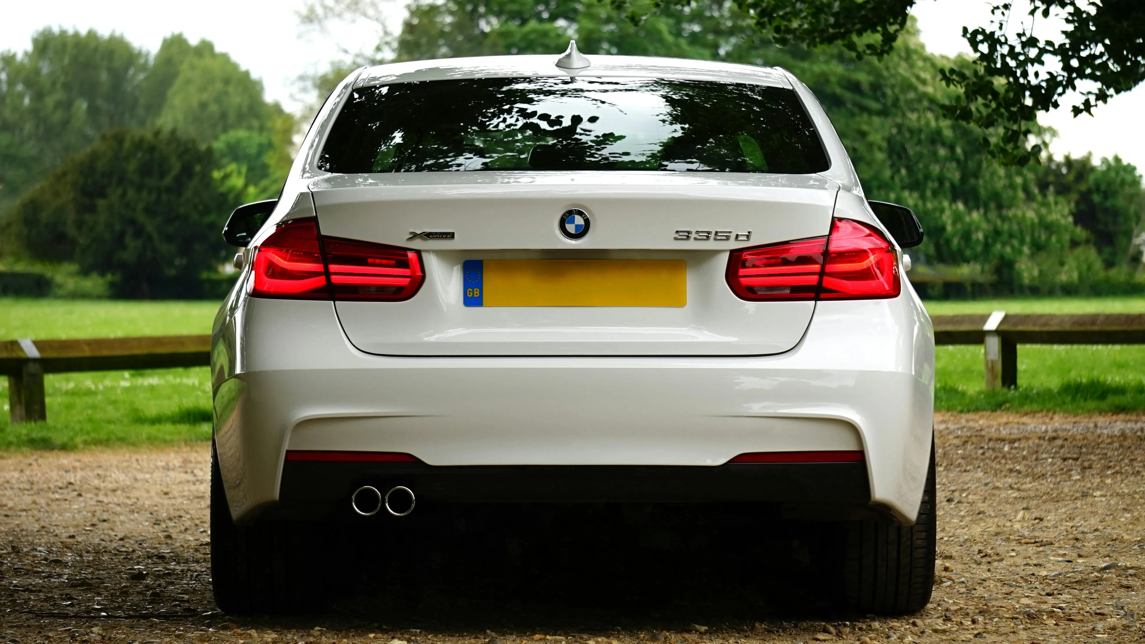 Rear View of White Bmw Parked on Grass with Trees Image