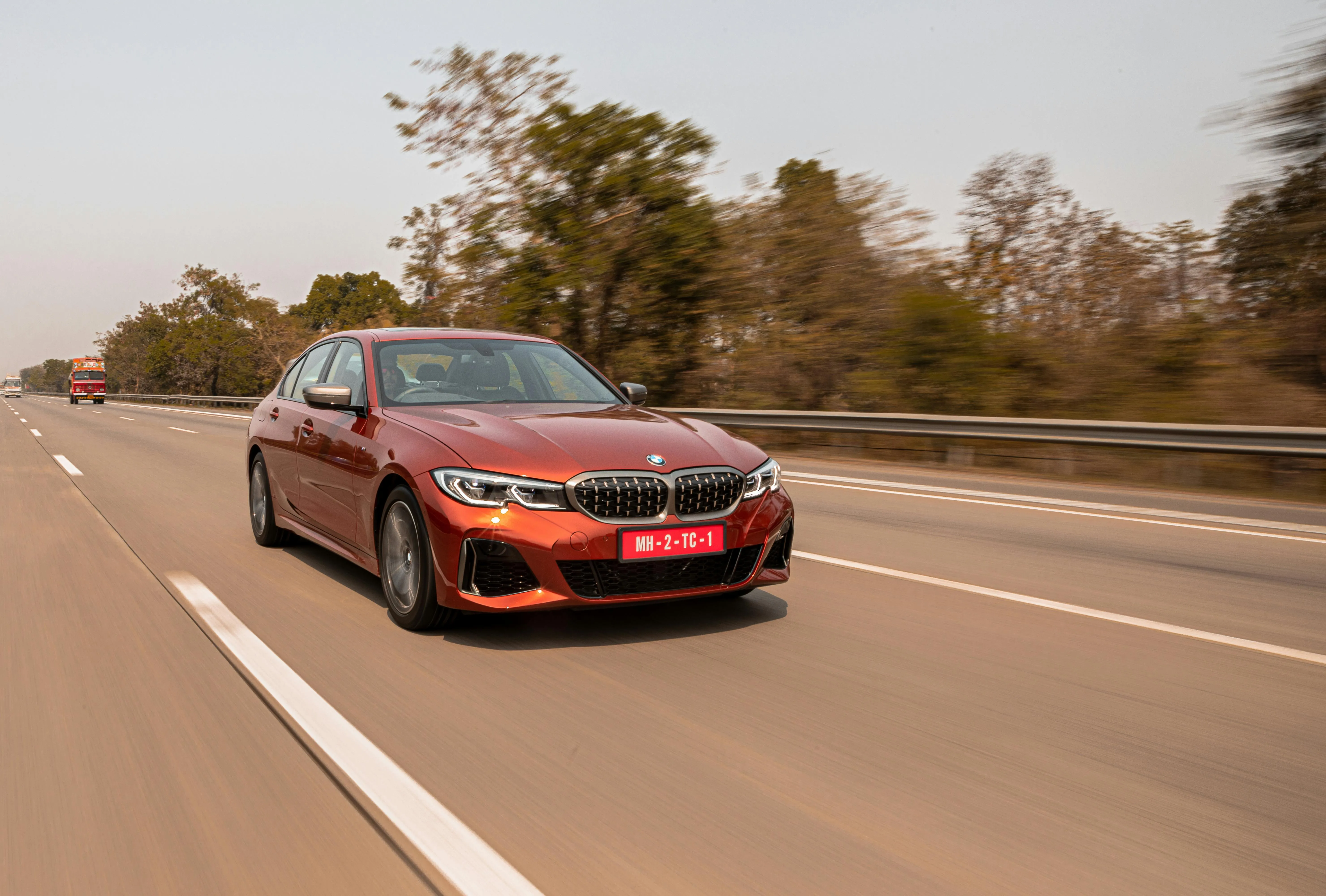 Red Bmw Driving Fast on Open Road with Trees Around