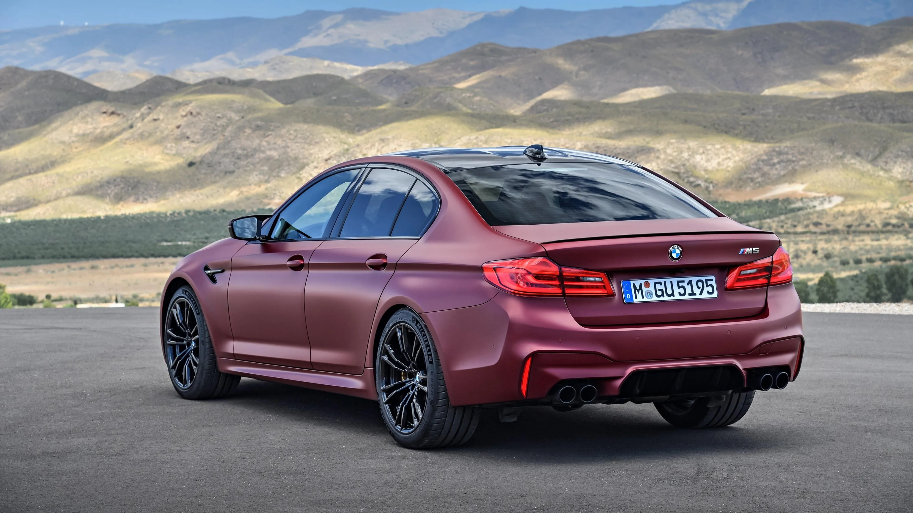 Red Bmw Driving Past Mountains Under Blue Sky Wallpaper