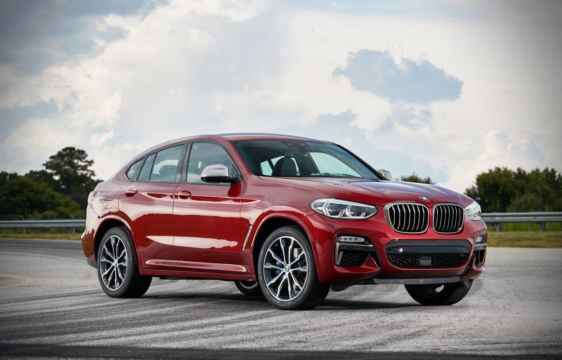 Red Bmw Suv Parked Near Hills Under Cloudy Sky View