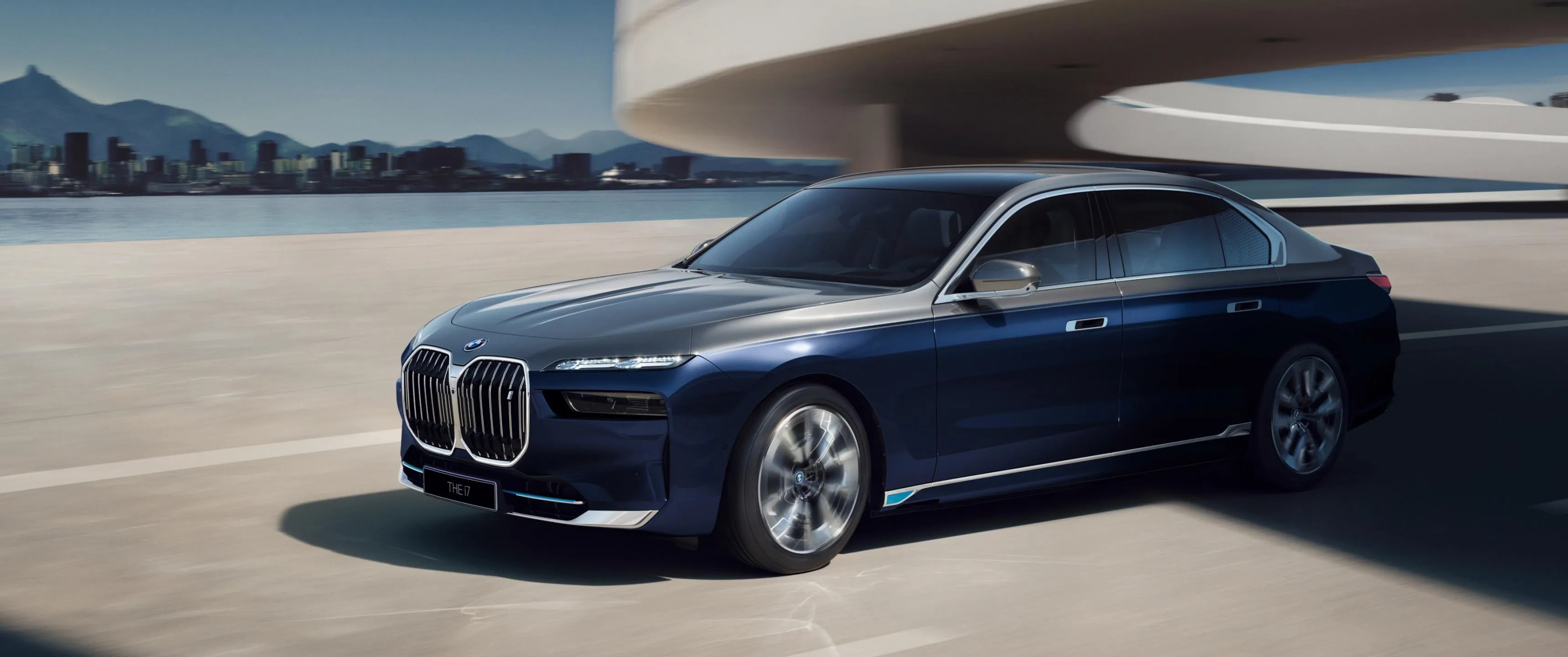 Silver Bmw Sedan Driving Along Coastal Road Under Sunlight