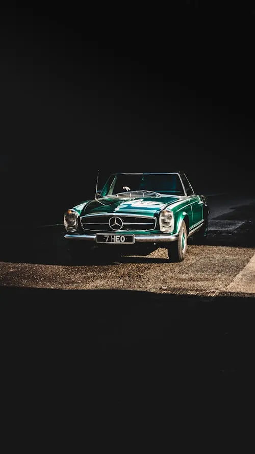 Vintage green Mercedes car driving on a dimly lit road