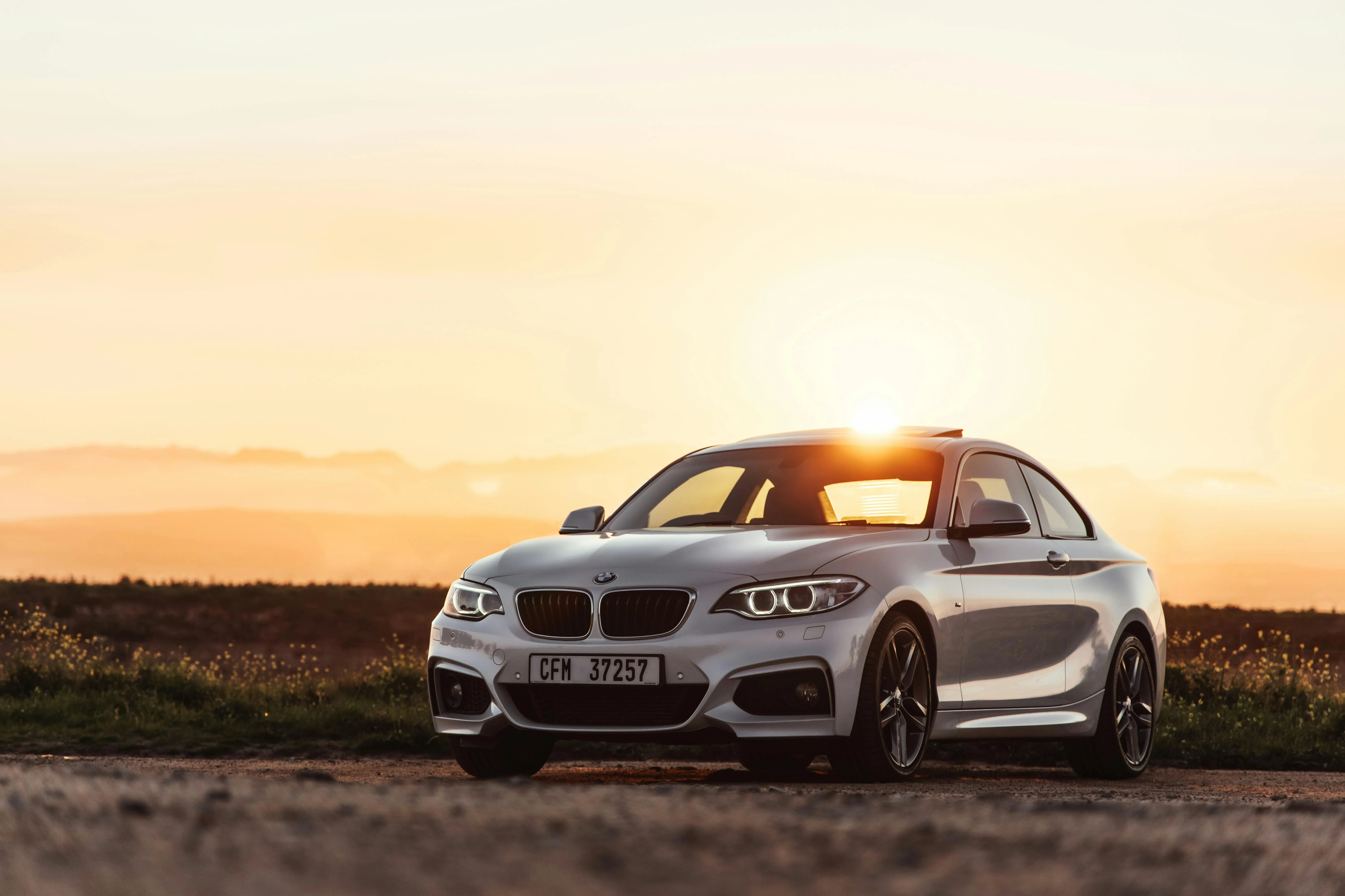 White Bmw Driving Into Sunset on Empty Road with Grass Sides