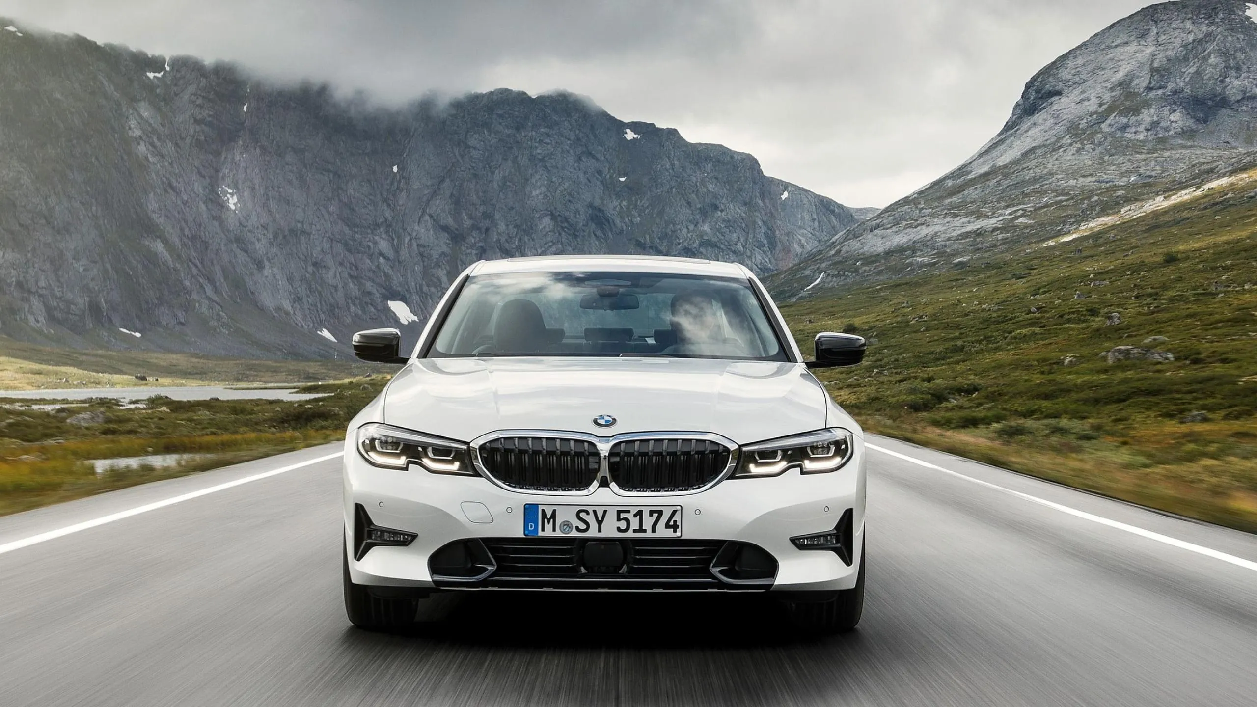 White Bmw Driving on Scenic Road with Mountains Ahead