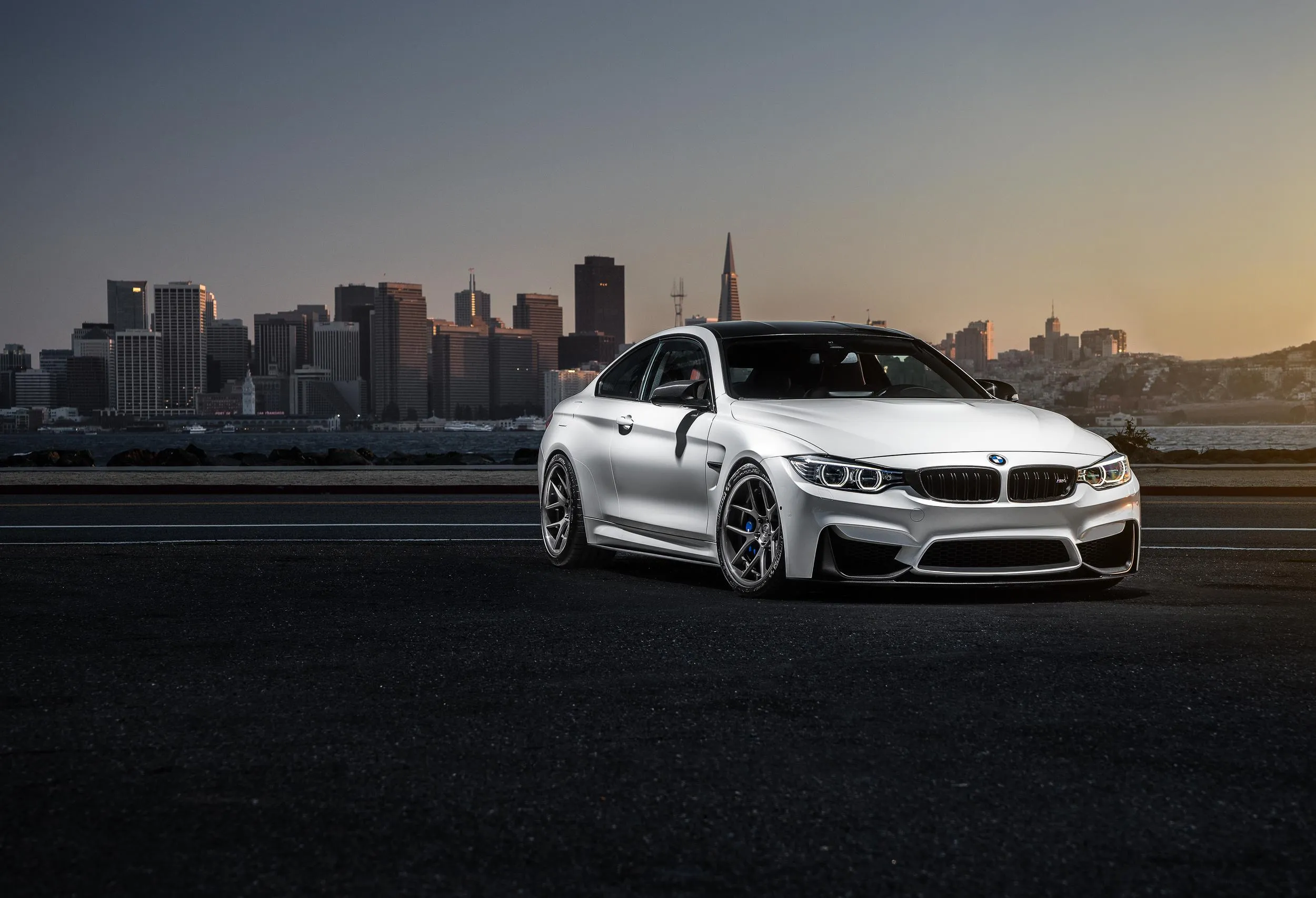 White Bmw Parked at Dusk with City Skyline Background