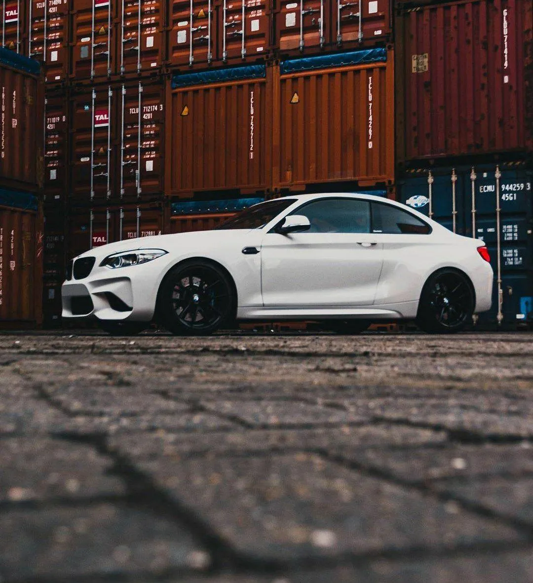 White Bmw Parked Beside Shipping Containers in Warehouse Area