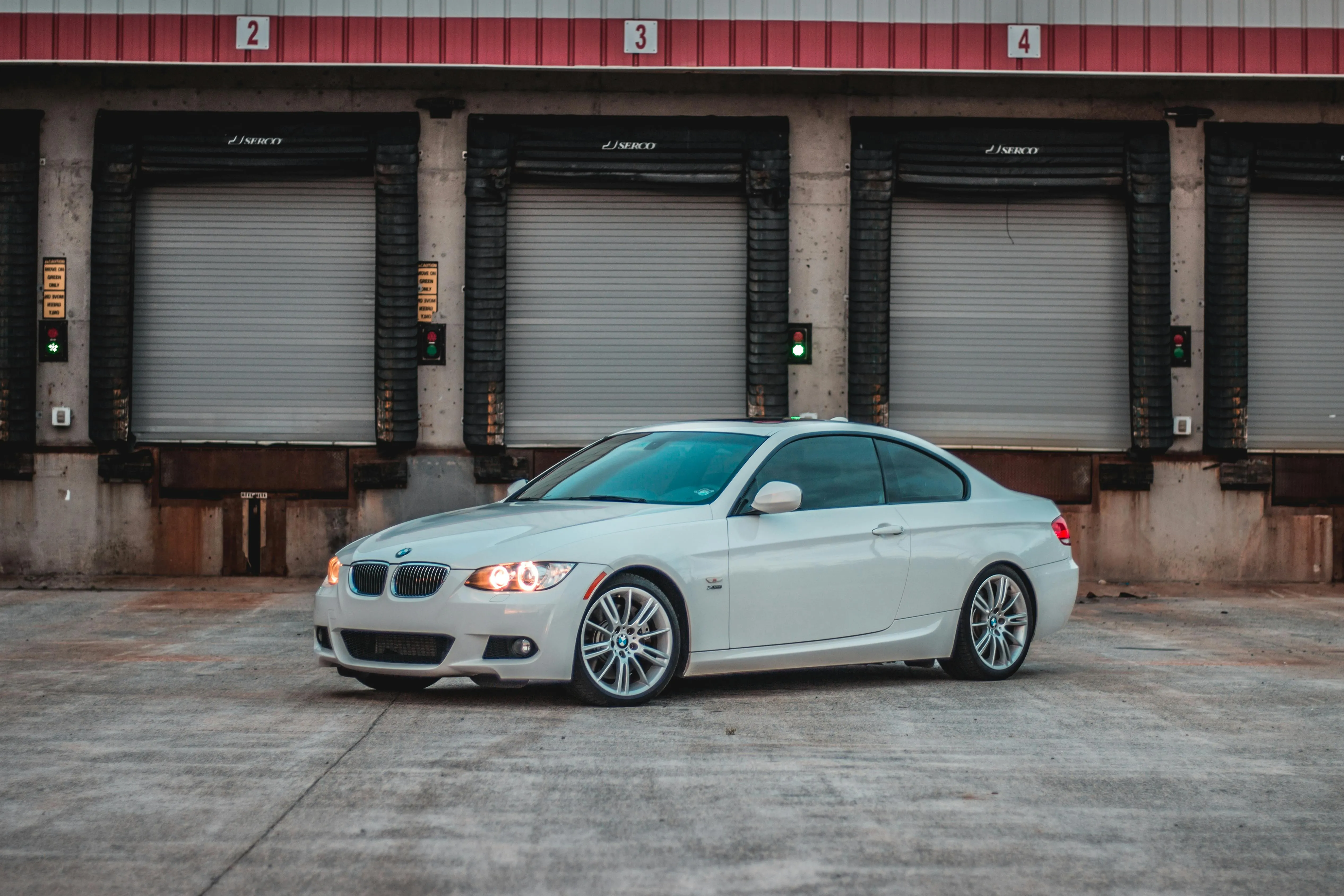 White Bmw Parked Outside a Warehouse with Red Rolling Doors