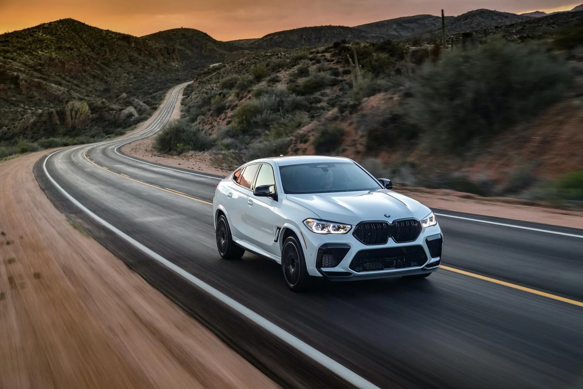 White Bmw Sedan Driving on a Curvy Desert Road at Sunset
