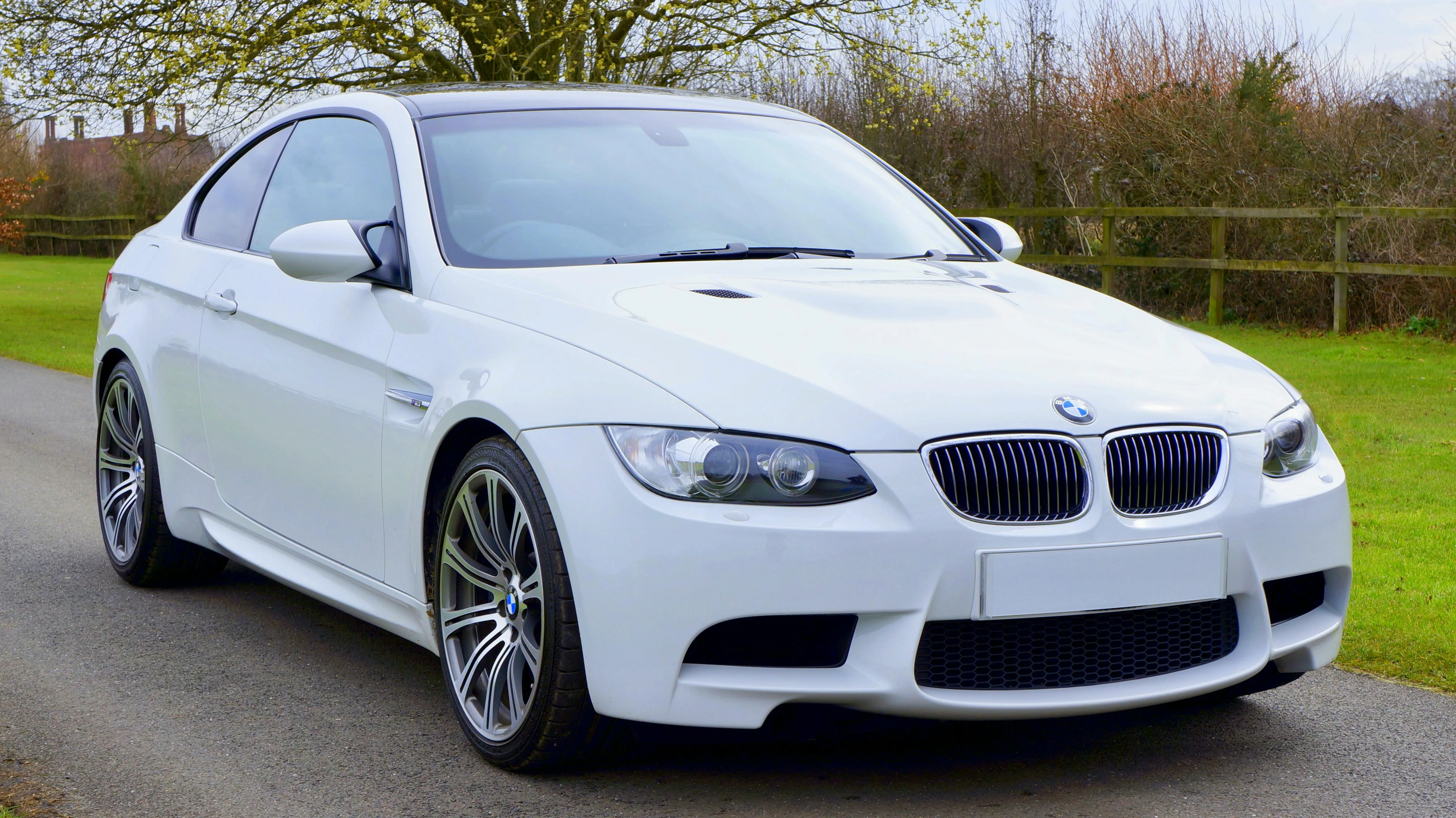 White Bmw Sedan Parked on Green Grass Near a Wooden Fence