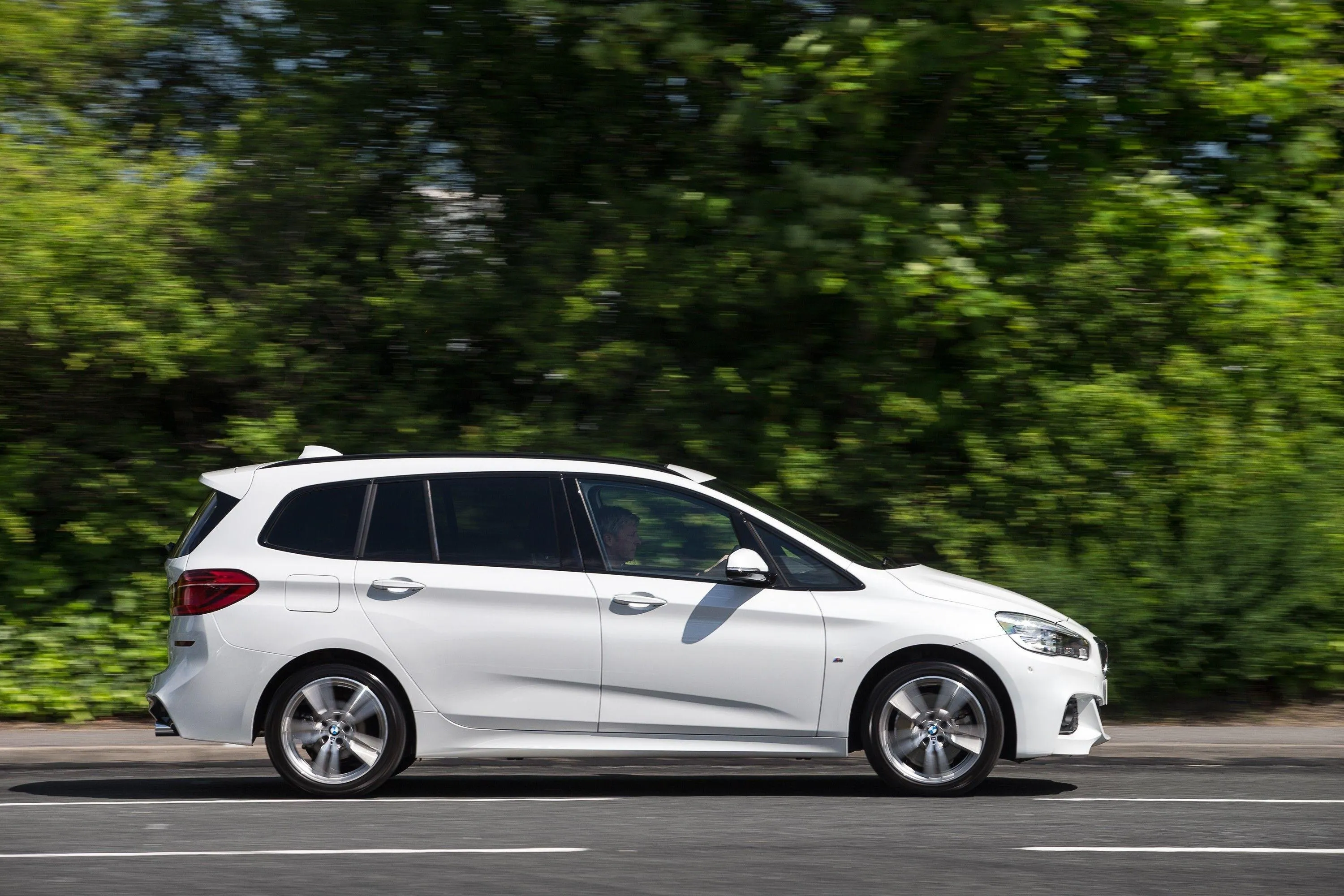 White Bmw Suv Driving on a Road Surrounded By Trees Image