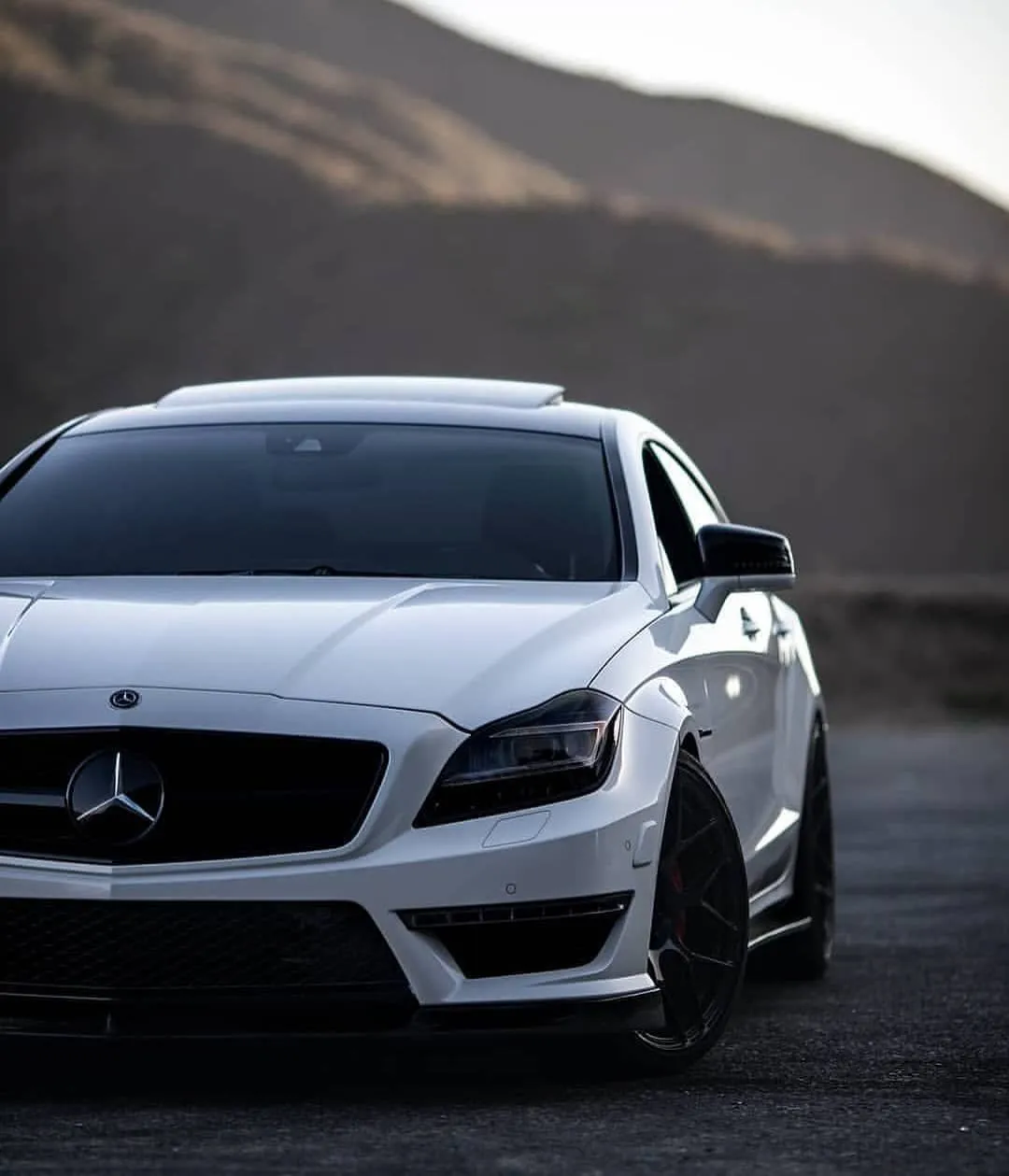 White Mercedes Benz on Dark Road With Hills Behind Wallpaper
